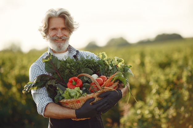 Free photo close up of old farmer holding a basket of vegetables. the man is standing in the garden. senior in a black apron.