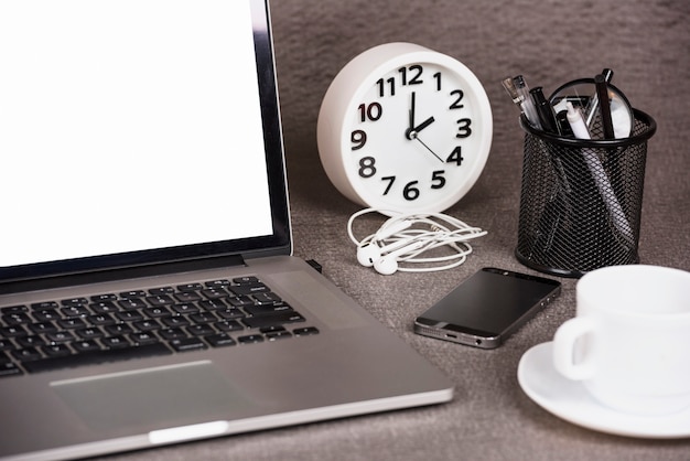 Close-up of an open digital tablet with alarm clock; cell phone and office supplies on desk