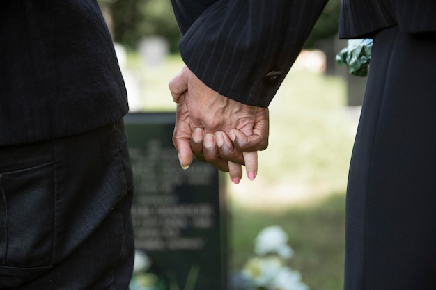 Close up people holding hands by the grave of loved one