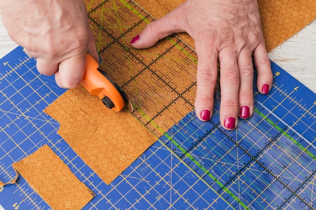 Free photo close-up of a person cutting fabric pieces by rotary cutter on mat using ruler