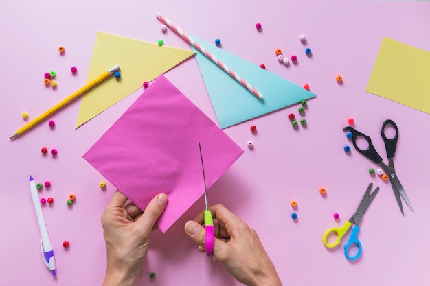 Close-up of a person cutting paper with scissor over the pink backdrop