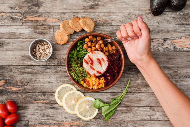 Free Photo close-up of a person eating the burrito bowl with bread and lime slices on wooden desk