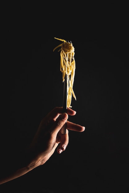 Close-up person holding fork with noodles 