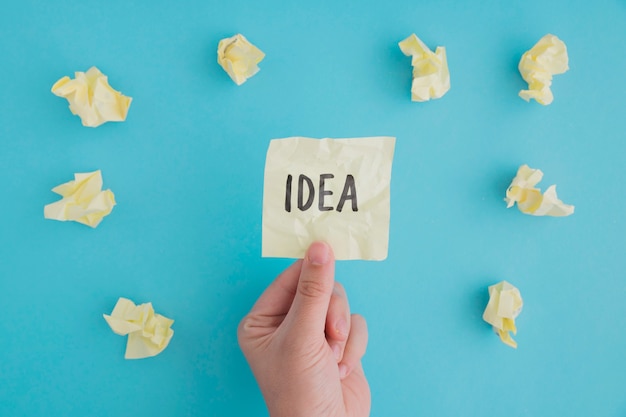 Free photo close-up of a person holding idea paper with crumpled ball of papers on blue backdrop