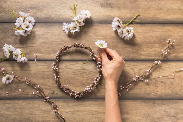 Free photo close-up of person making flower and twig wreath on wooden table