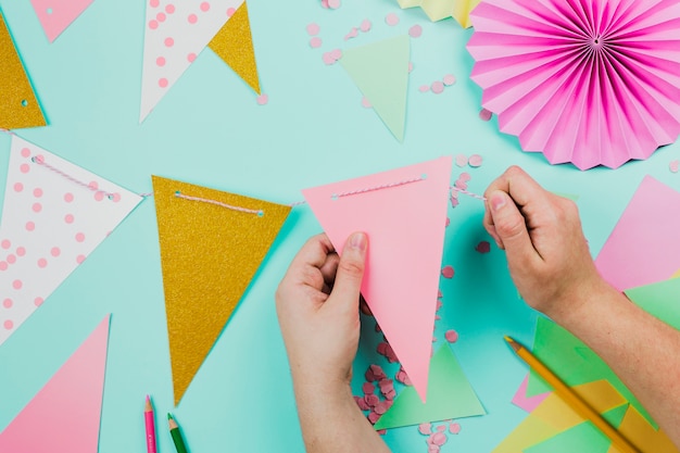 Free Photo close-up of a person preparing the bunting with triangular paper and confetti on teal background