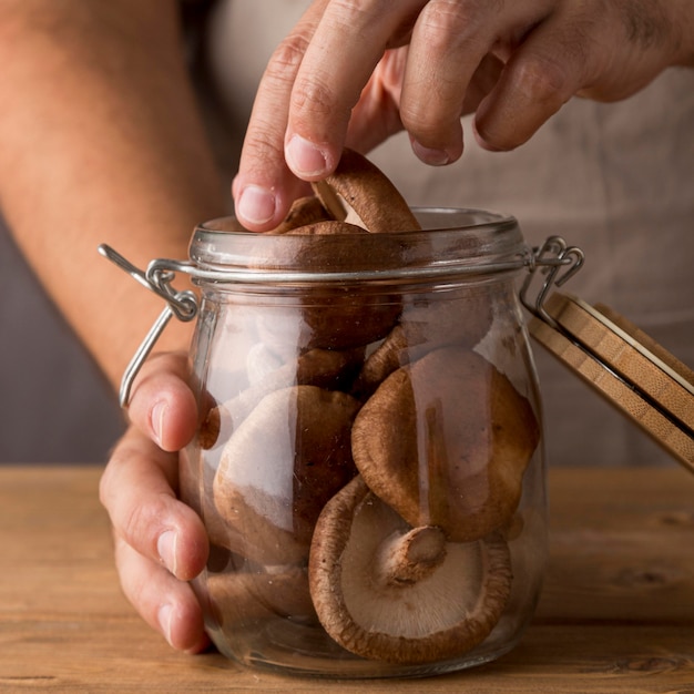 Close-up of person putting mushrooms in glass jar