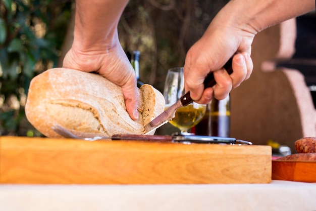 Free photo close-up of a person's hand cutting loaf of bread on chopping board