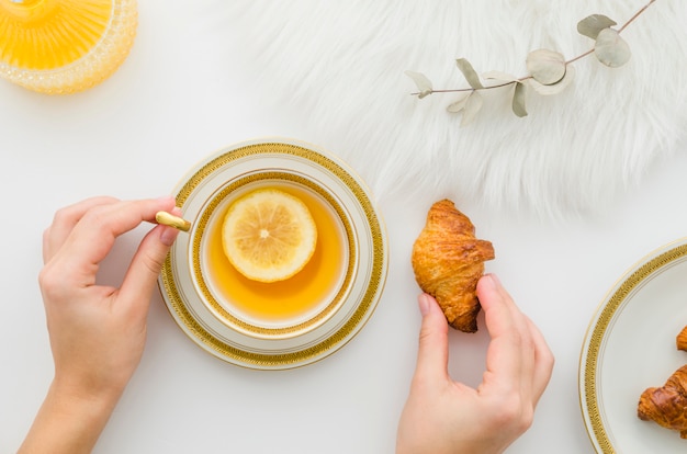 Close-up of a person's hand having croissant with lemon tea on white background