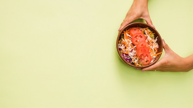 Close-up of a person's hand holding bowl of salad on mint green background