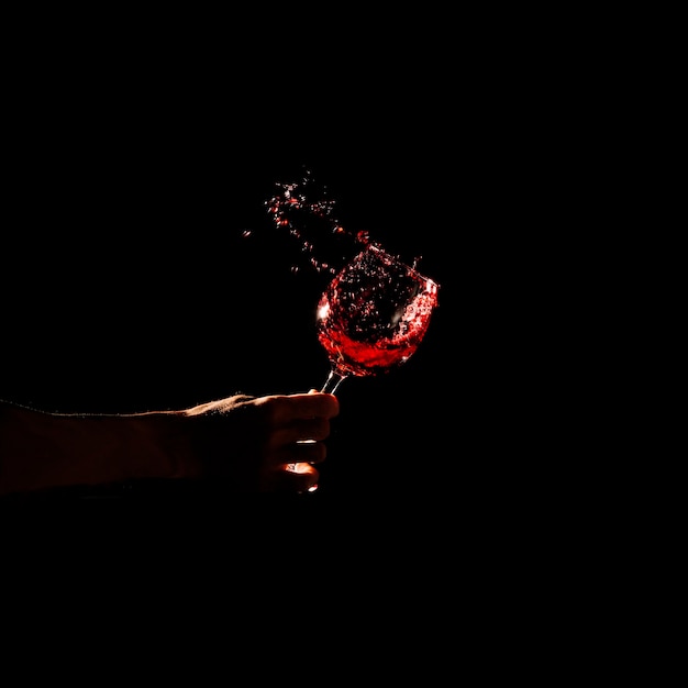 Close-up of a person's hand holding glass of red wine splashing out of glass