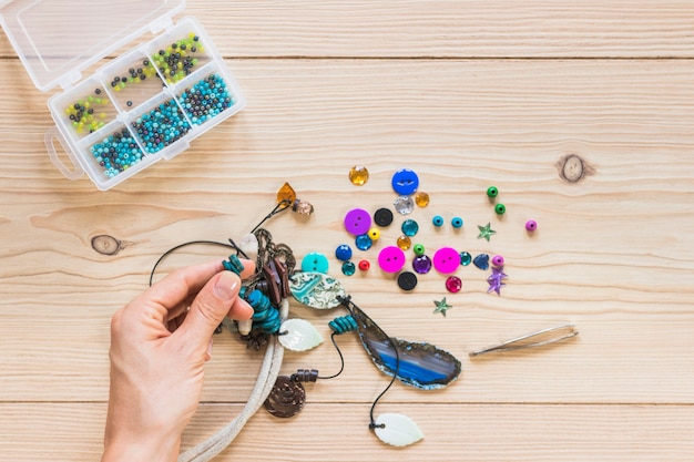 Free Photo close-up of person's hand making handmade jewelry on wooden table