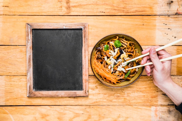 Free photo close-up of a person's hand picking the noodles with chopsticks near the blank slate on table