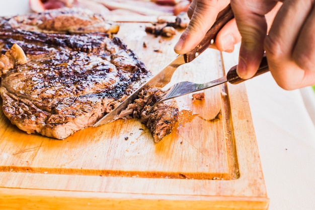 Free photo close-up of a person's hand slicing meat with fork and knife