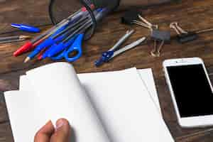 Free photo close-up of person's hand turning white paper with stationeries and cellphone