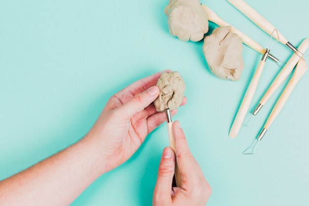 Close-up of a person's hand using sculpting tools on mint green background