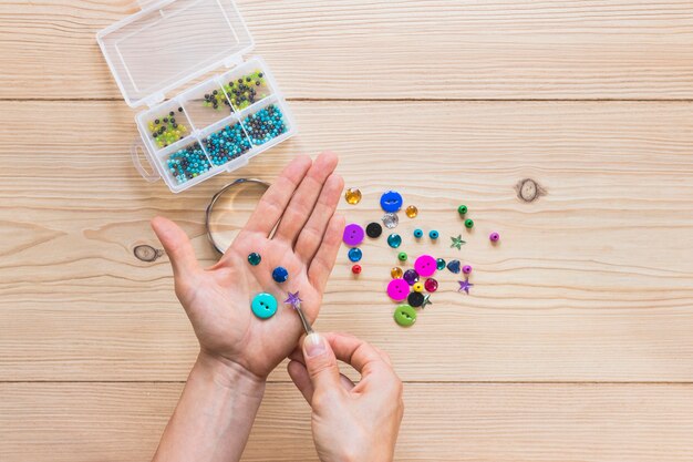 Close-up of a person's holding beads and button with tweezers