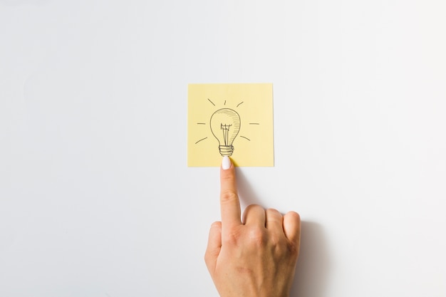 Close-up of a person touching finger on drawn light bulb over the sticky note