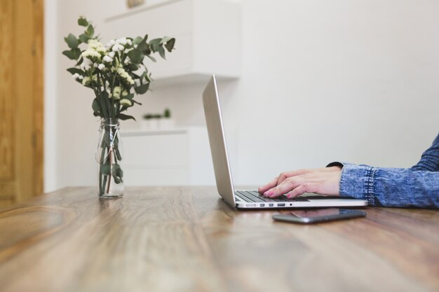 Close-up of person using her laptop on a wooden table