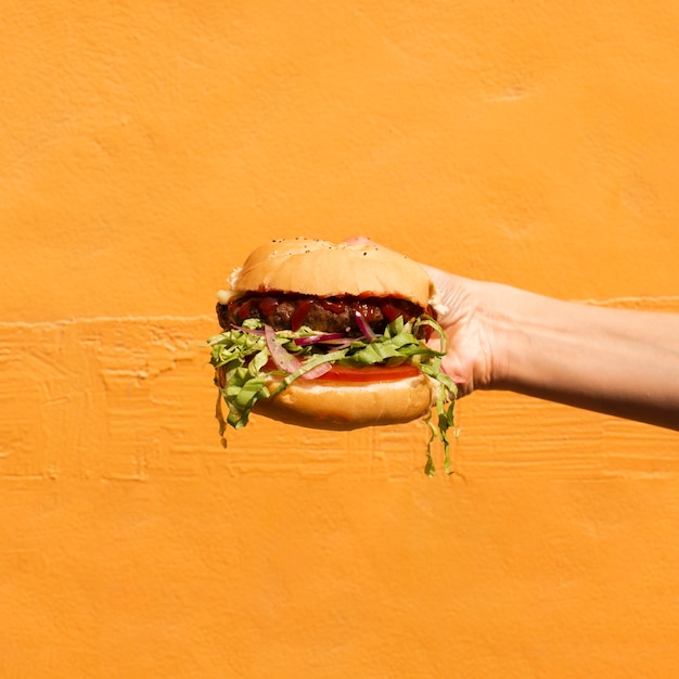 Free photo close-up person with burger and orange background