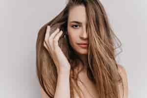 Free photo close-up photo of adorable young woman gently touching her hair. indoor portrait of blissful beautiful woman isolated.