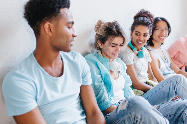 Close-up photo of african boy in blue shirt looking at pretty girls wears denim pants. Indoor portrait of students talking about their studies with interest..