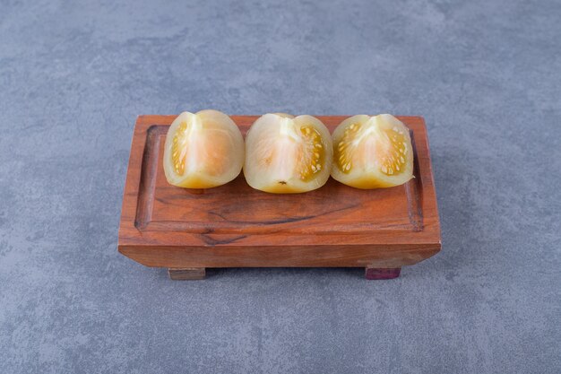 Close up photo of canned green tomato slices on wooden board.