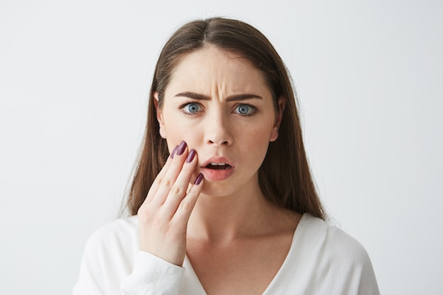 Free Photo close up photo of displeased frightened girl touching face frowning .