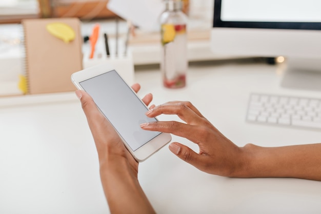 Close-up photo of female hands holding white phone under table