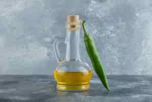 Free photo close up photo of green hot pepper with bottle of oil on grey background