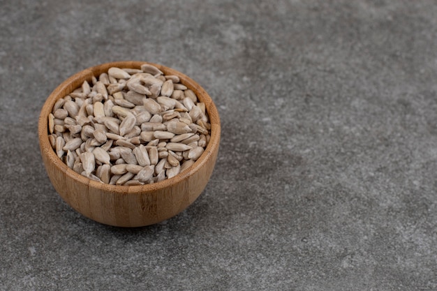 Close up photo of Peeled sunflower seeds in wooden bowl over grey surface. 