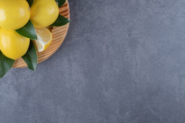 Close up photo of pile of lemons on wooden plate.