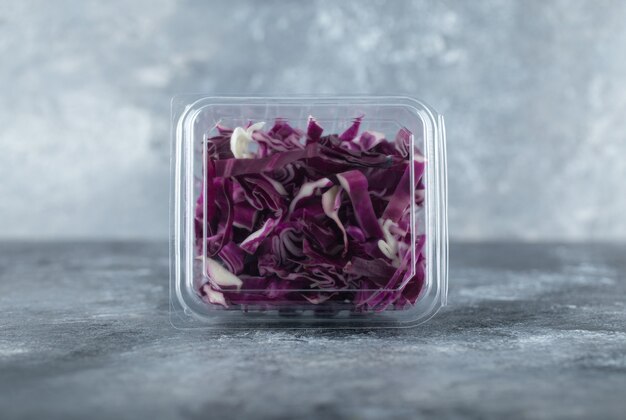 Close up photo of plastic container full with chopped purple cabbage o grey background. 