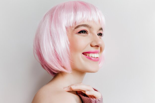 Close-up photo of refined caucasian girl with dark eyes happy laughing. Indoor portrait of stunning young woman in pink periwig enjoying life.