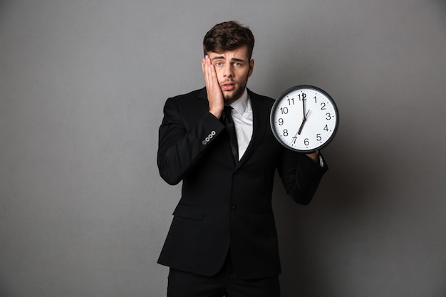 Free photo close-up photo of upset worker in suit holding clock,