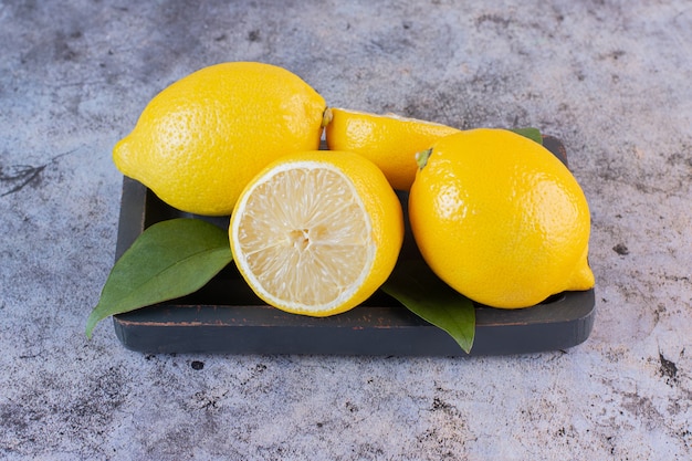 Close up photo of whole or half cut lemons on wooden plate.