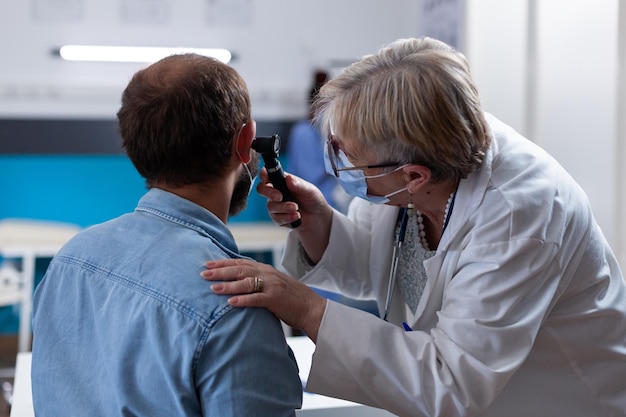 Free photo close up of physician using otoscope to do ear consultation with patient. woman otologist checking infection with otolaryngology instrument at medical visit during coronavirus pandemic.