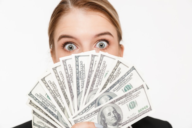 Close up picture of shocked blonde business woman hiding behind the money and  over white wall