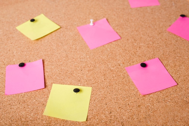 Free photo close-up of pink and yellow adhesive notes on corkboard