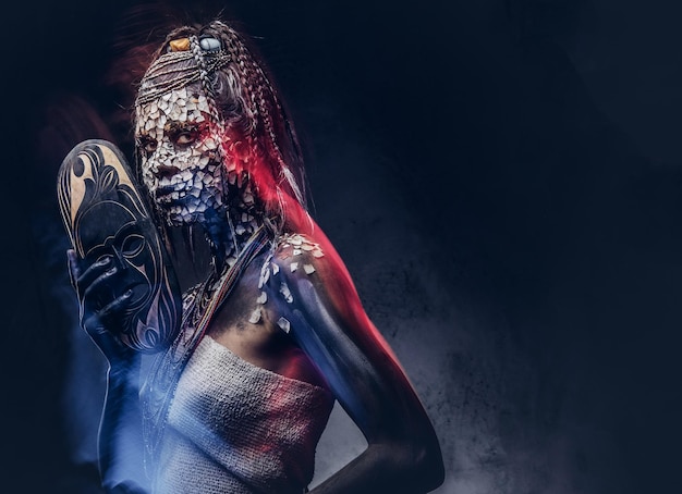 Close-up portrait of an African shaman female from the indigenous African tribe, wearing traditional costume. Make-up concept. Isolated on a dark background.