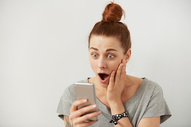 Close up portrait anxious or shocked young freelancer woman looking at phone seeing bad news