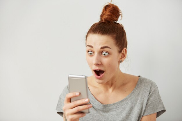 Close up portrait anxious or shocked young freelancer woman looking at phone seeing bad news