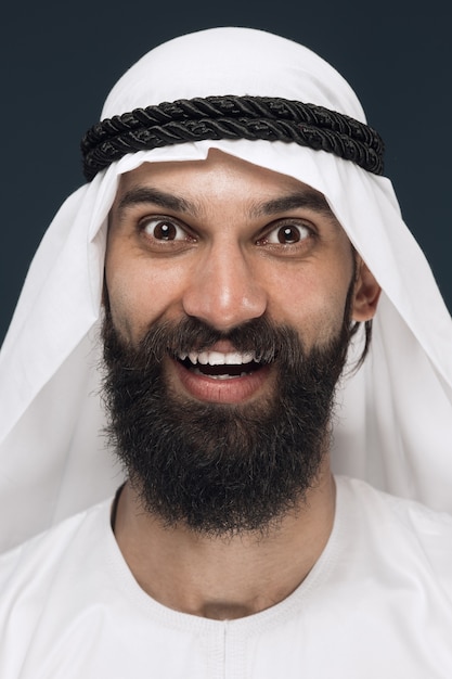 Free Photo close up portrait of arabian saudi businessman on dark blue studio background. young male model standing and smiling, looks happy. concept of business, finance, facial expression, human emotions.