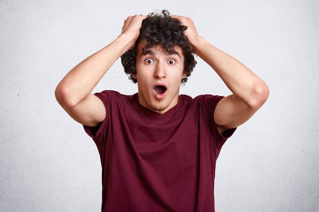 Close up portrait of astonished young man keeps hands on head