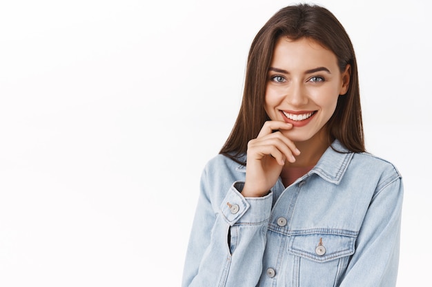 Close-up portrait attractive sensual, feminine woman with lovely smile, touching lip and giggle coquettish as standing over white background in denim jacket, express flirt and seduction