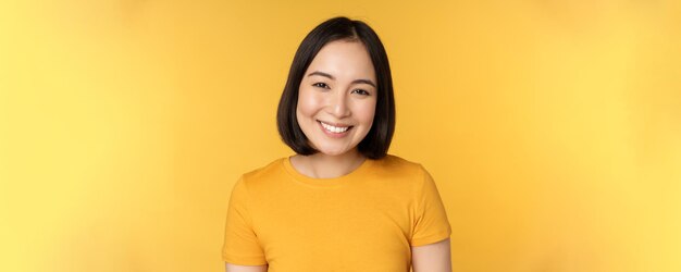 Close up portrait of beautiful asian woman smiling looking cute and tender standing against yellow b