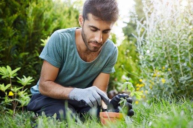 Free Photo close up portrait of beautiful bearded hispanic male gardener concentrated planting sprout in flower pot with garden tools, enjoying moments of silence.