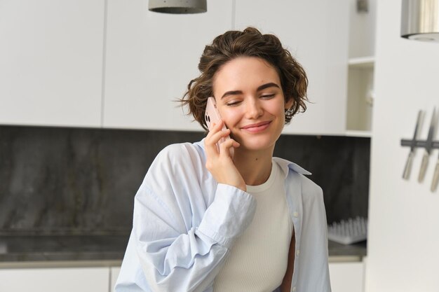 Close up portrait of beautiful european girl with smartphone sitting at home and talking on mobile p