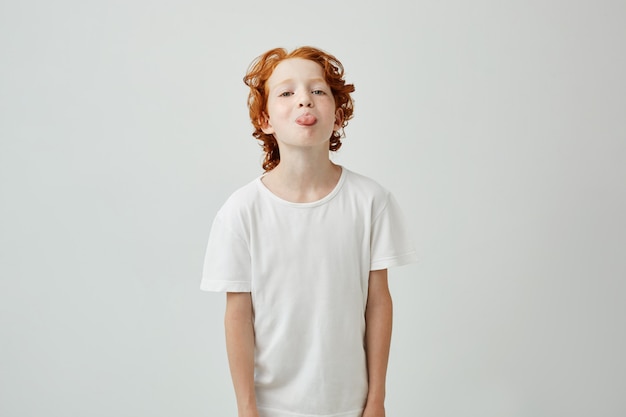 Free photo close up portrait of beautiful ginger kid in white t-shirt showing tongue