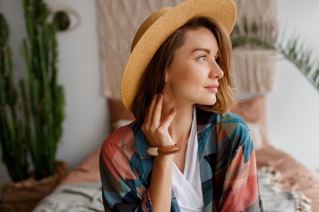 Close up portrait of beautiful romantic woman in straw hat chilling over bohemian interior